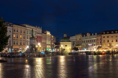Krakow, Polonya - 18 Temmuz 2016: Kaldırımda bir sürü eski ev ve yansımalarla aydınlanan ana meydanın gece görüşü