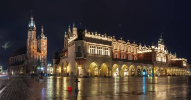 Krakow, Polonya - 18 Temmuz 2016: Geniş bir katedral ve pazar binası ve kaldırımda birçok eski ev ve yansıması bulunan aydınlık ana meydanın gece görüntüsü