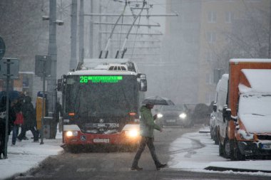 Brno, Çek Cumhuriyeti - 26 Kasım 2021: Şiddetli bir kar yağışı altında ışıkları açık bir tramvay, insanlar iniyor ve diğer arabalar onu bekliyor.