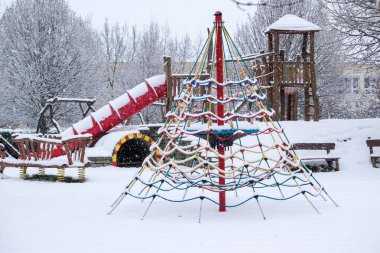 Kış karlı oyun parkı. Ahşap çocuk şatosundan kayan kırmızı bir tünel. Renkli tırmanma ağı.
