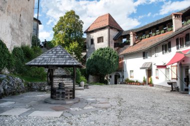 Courtyard of the castle at Lake Bled in Slovenia. Old buildings, stone paving and a wooden fountain in the middle of the square.