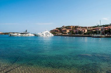 Porto Cervo, İtalya - liman kıyısı ve Sardunya adasında eski evler. Kristal berrak denizde demirlemiş büyük lüks yatlar..