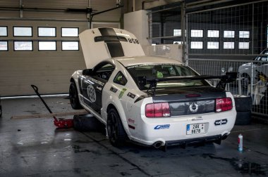 Beyaz, hızlı spor araba (Ford Mustang), Brno 'daki bir yarışa hazırlanırken krikonun üzerinde duruyor. Arka görünüm.