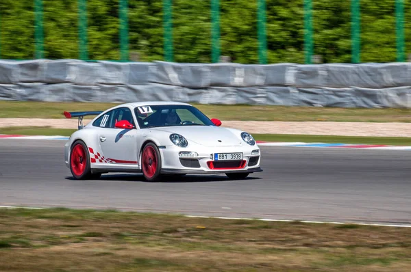 Beyaz bir spor araba (Porsche 911) bir yarış pistine biner. Asfalt yolda hızlı sürüş.