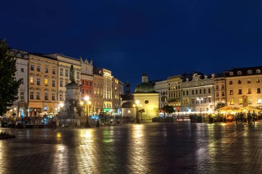 Krakow, Polonya - 18 Temmuz 2016: Kaldırımda bir sürü eski ev ve yansımalarla aydınlanan ana meydanın gece görüşü