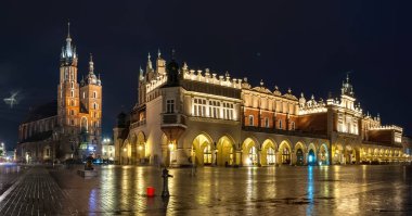 Krakow, Polonya - 18 Temmuz 2016: Geniş bir katedral ve pazar binası ve kaldırımda birçok eski ev ve yansıması bulunan aydınlık ana meydanın gece görüntüsü