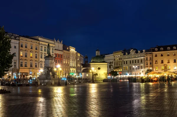 Krakow, Polonya - 18 Temmuz 2016: Kaldırımda bir sürü eski ev ve yansımalarla aydınlanan ana meydanın gece görüşü