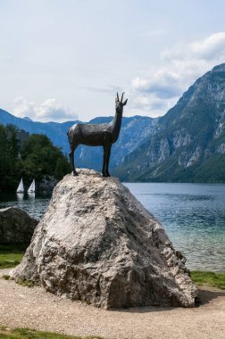Slovenya 'daki Bohinj Gölü. Sahildeki bir kayanın üzerinde duran bir papağan heykeli..