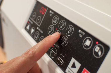 Başlatma düğmeleri olan makine kontrol paneli yazdırılıyor. İşçi eli, parmak güç düğmesine basıyor..