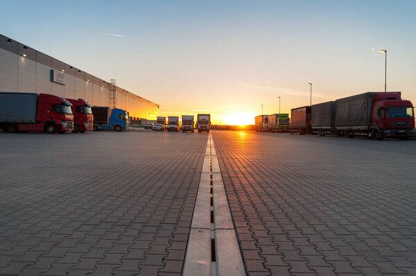 Логистическая зона с залами и грузовиками на закате. Транспортировка и хранение грузов.