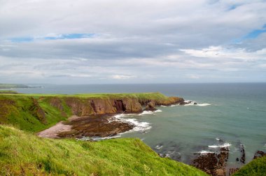 İskoçya 'nın doğusunda deniz kıyısında çimlerle kaplı kayalar.