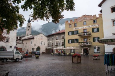 Glorenza, Italy - 26 August 2013: Square in the rain in the city of Glorenza in Italy in the mountains in summer. Old houses with shops, church tower and wet paving on the ground.