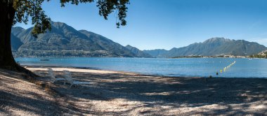 Lake Locarno - lake shore with pebble beach and high mountains of swiss alps in the background.