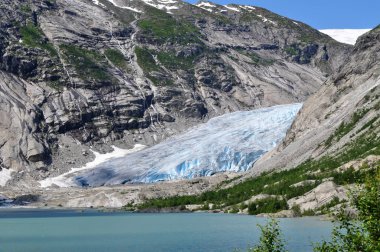 Norveç 'teki bir gölün üzerindeki kayalık dağların ortasındaki devasa Jostedalsbreen buzulu.