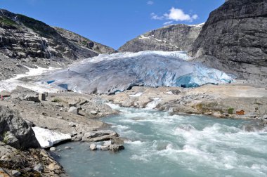 Norveç 'teki bir gölün üzerindeki kayalık dağların ortasındaki devasa Jostedalsbreen buzulu.