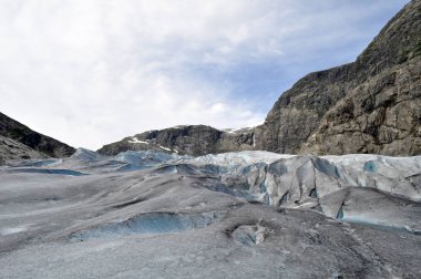 Norveç 'teki bir gölün üzerindeki kayalık dağların ortasındaki devasa Jostedalsbreen buzulu.
