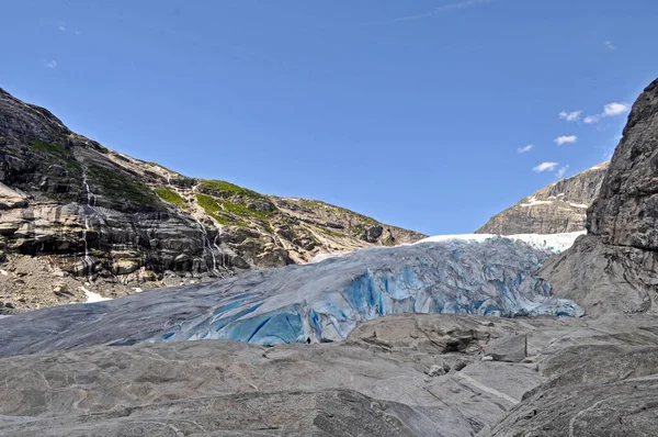 Norveç 'teki bir gölün üzerindeki kayalık dağların ortasındaki devasa Jostedalsbreen buzulu.