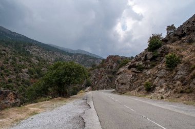 An asphalt road leads through the mountains on the island of Corsica. Stony rocks on hills.