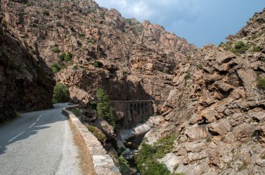 An asphalt road leads through the mountains on the island of Corsica. Stony rocks on hills.