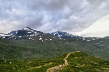 Karlı dağlarla kaplı tepe manzarası ve Norveç 'te yürüyüş yolu. Dağların üzerinde bulutlar.