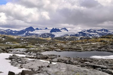 Norveç 'te yazın ortasında karlı bir manzara. Karlı dikenli dağlar, donmuş bir göl ve her yer karla kaplı..
