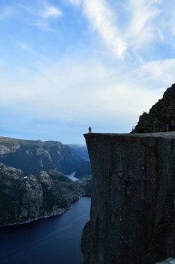 Norveç, Preikestolen, İskandinavya 'da bir fiyordun üzerinde yüksek bir kayanın üzerinde küçük bir adam. Dağlar ve deniz üzerindeki doğa.