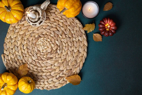 Holiday Thanksgiving table setting background. Top view of wicker place mat, pumpkins, autumn leaves, candle on dark table. Autumn table setting. Restaurant menu. Copy spac