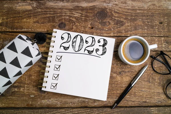 Yeni yıl hedefleri 2023 masada. Ahşap arka planda defter, kahve fincanı ve gözlüklü 2023 karar listesi. Hedefler, plan, strateji, iş, fikir, eylem konsepti