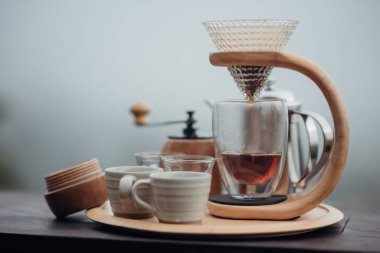 Çelik çaydanlık, bardak ve el damlası ile damlayan kahve seti. Sis ve doğa arka planıyla minimalist tarzda kahve makinesi..