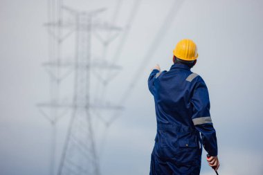 Sarı kasklı bir erkek güç mühendisi yüksek voltajlı elektrik hattının altındaki güç hattını kontrol ediyor..