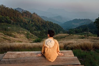 Yalnız bir adam ahşap balkonda oturuyor ve Hadubi, Chiang Mai, Tayland 'daki sıradağlara bakıyor..