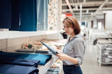 Asyalı bir kadın alışveriş merkezinde kumaş ve tekstil seçiyor..