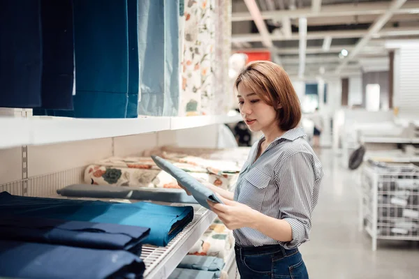 Asyalı bir kadın alışveriş merkezinde kumaş ve tekstil seçiyor..
