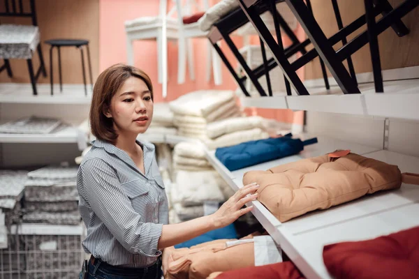 An Asian woman is selecting a seat cushion at the mall.