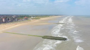 Belçika 'nın Middelkerke sahil kasabasının sahil şeridindeki insansız hava aracı videosu yaz mevsiminde dalgalı sularda yüzüyor.
