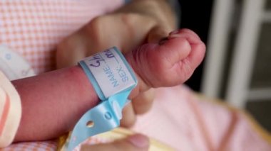 Yeni doğmuş bebek annesinin parmağını tutuyor. Elinde isim bandıyla yeni doğmuş bir bebek..