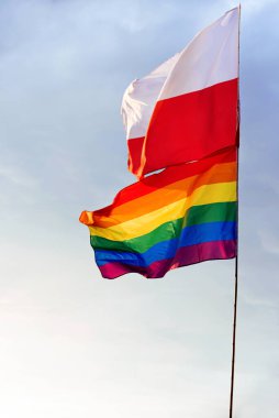Polonya ve LGBT renklerine sahip gökkuşağı bayrağı beyaz bulutlu mavi gökyüzünün arka planına karşı