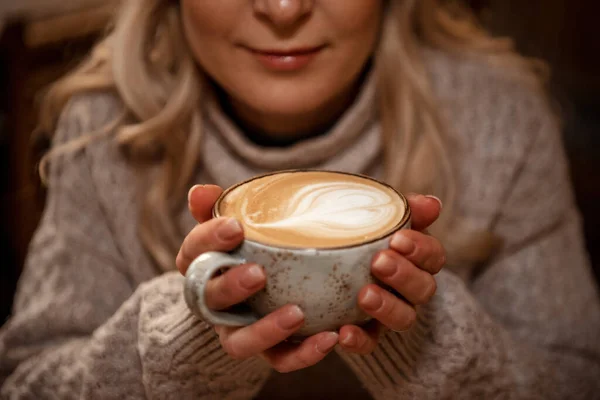 Trendy cool woman or young girl  holds take away to go cup of coffee with milk latte art, concept life on the go, warm and cosy drink.