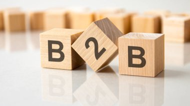 Gri bir masanın parlak yüzeyinde B2B harfleri olan üç tahta küp. Küplerdeki yazıtlar masanın yüzeyinden yansıyor. b2b - ticaretin kısaltılmışı
