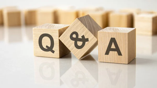 グレーのテーブルの明るい表面にQとAの文字を持つ3つの木製の立方体 立方体の碑文は表の表面から反映されています QとA 質問と回答のための短い — ストック写真
