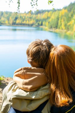 Romantik çift sonbahar parkında dinleniyor, sarılıyorlar, temiz havanın tadını çıkarıyorlar, güzel doğa, güzel sonbahar havası. Sevgililer birlikte vakit geçirir. Dikiz aynası. Sarı yapraklar, arka planda göl