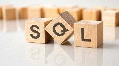 Gri bir masanın parlak yüzeyinde SQL harfleri olan üç tahta küp. Küplerdeki yazıtlar masanın yüzeyinden yansıyor. SQL - Yapılandırılmış Sorgu Dili 'nin kısaltması