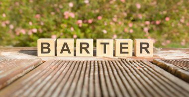 Takas kelimesi tahta küplere yazılmıştır. Taşlar güneş tarafından aydınlatılan eski bir tahta üzerine konur. Arka planda parlak çiçek açan bir çalı var.