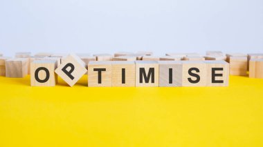 İyimser kelimesi, sarı bir masanın üzerinde duran tahta küplerden oluşur. Küplerden biri kenarlara, gri arka plana, iş konseptine yerleştiriliyor.