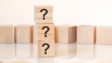 Dikey piramitte sıralanmış üç soru işaretli tahta küpler, sarı arka plan, masanın yüzeyinden yansıma, iş konsepti