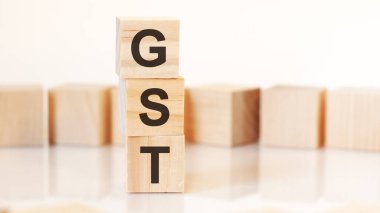 Üzerinde GST harfleri olan tahta küpleri dikey bir piramide yerleştirilmiş, arka planda, yansıma yüzeyi, iş konsepti. Mal ve Hizmetler Vergisinin GST kısaltması