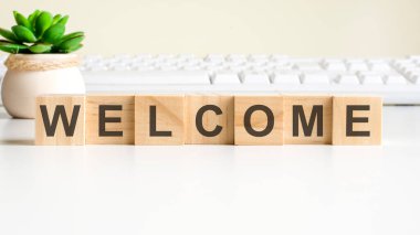 Tahta bloklardan yapılmış hoş geldin kelimesi. Ön görünüm kavramları, vazodaki yeşil bitki ve arkaplanda beyaz klavye