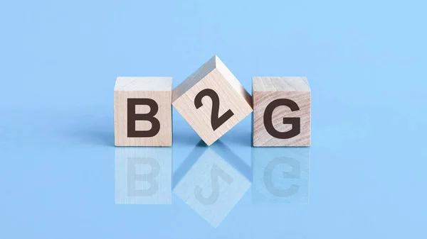 B2Gは政府へのビジネスの略語です テキストは木製の立方体に書かれています 立方体の1つは端に立っています 青の背景 — ストック写真