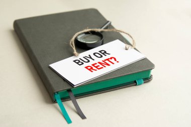 Gri defterde bir büyüteç ve üzerinde seçici odaklı Buy or Rent yazan beyaz bir kağıt var.