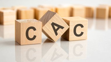 Gri bir masanın parlak yüzeyinde CAC harfleri olan üç tahta blok. Küplerdeki yazıtlar masanın yüzeyinden yansıyor. cac - müşteri edinme maliyeti